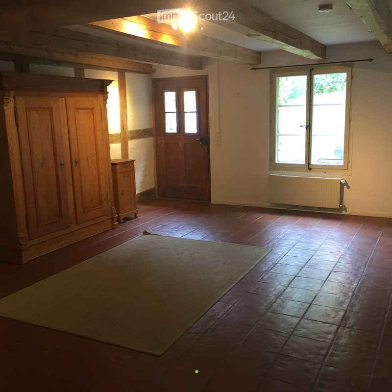 Empty room with wooden floor, exposed wooden beams, large window, wooden cabinet, and door.
