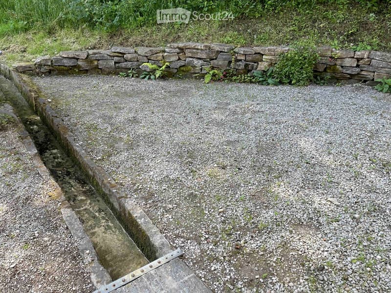 Gravel pathway bordered by stone walls, with small water channel on one side and greenery on the other.