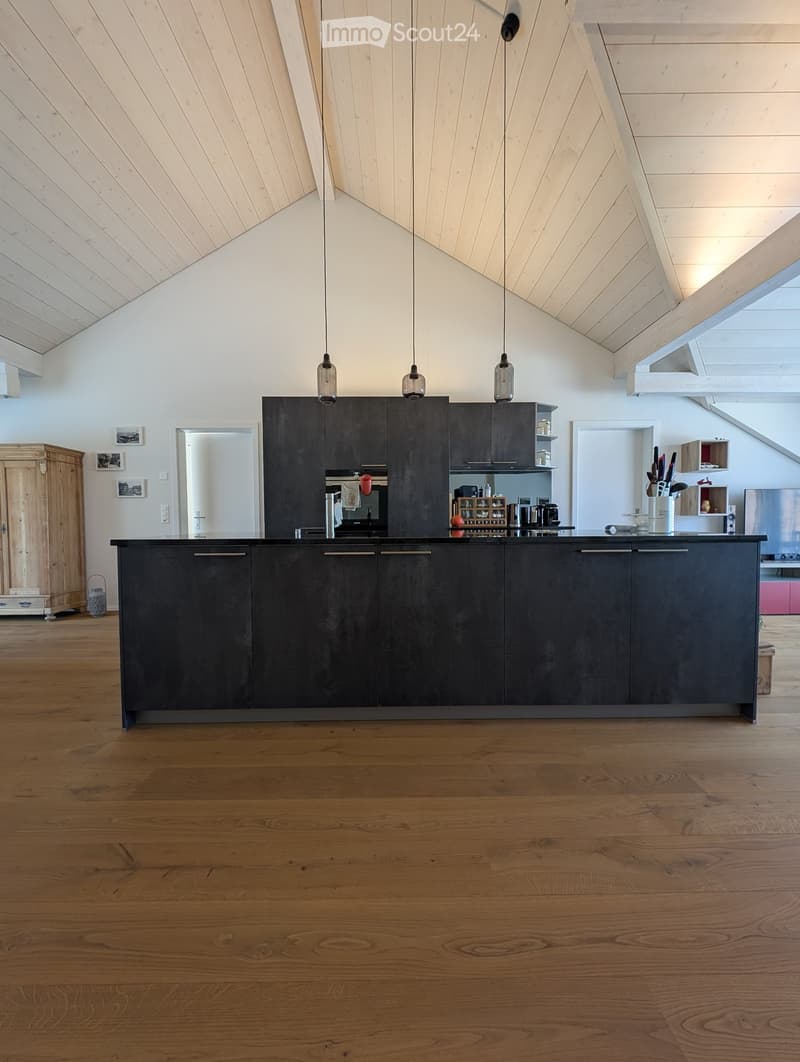 Modern kitchen with dark grey cabinets, a central island, pendant lights, and wooden flooring.