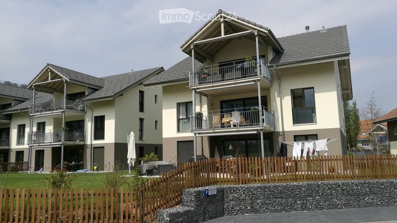 Modern two-story residential building with balconies, large windows, and a fenced garden area.