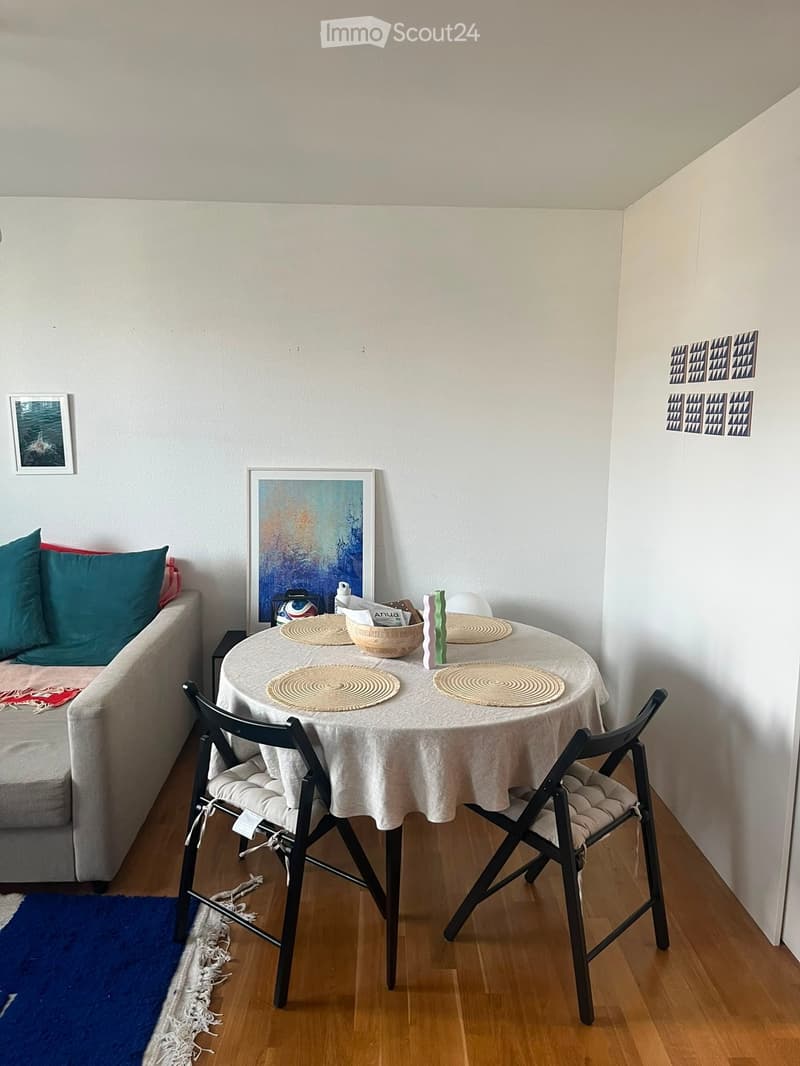 A small, cozy living space with a sofa, a round table with chairs, and decorative items including a picture frame and artwork on the walls.