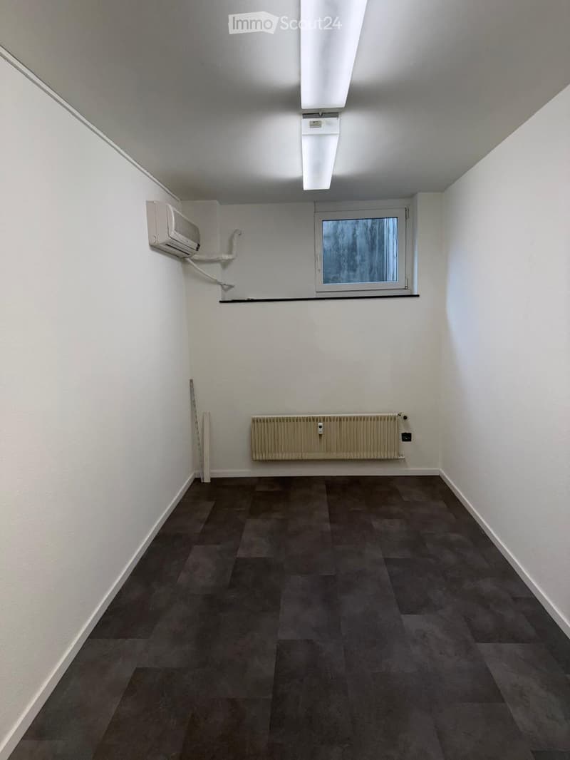Empty room with white walls, dark tiled floor, window with frosted glass, radiator, and air conditioning unit on the wall.