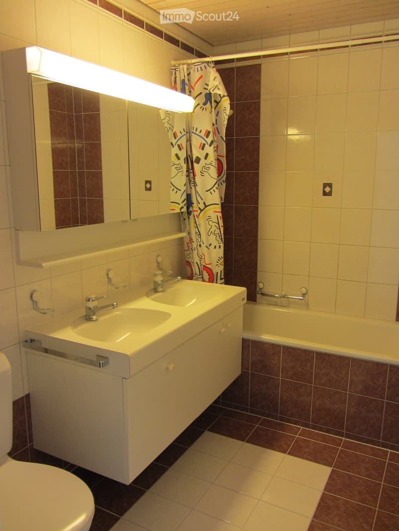 Modern bathroom with double sink, mirror, bathtub, and shower curtain. Features tiled walls and floor in neutral tones.