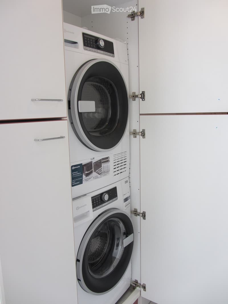A compact, modern bathroom with a built-in washing machine and dryer unit, white cabinetry, and sleek design.