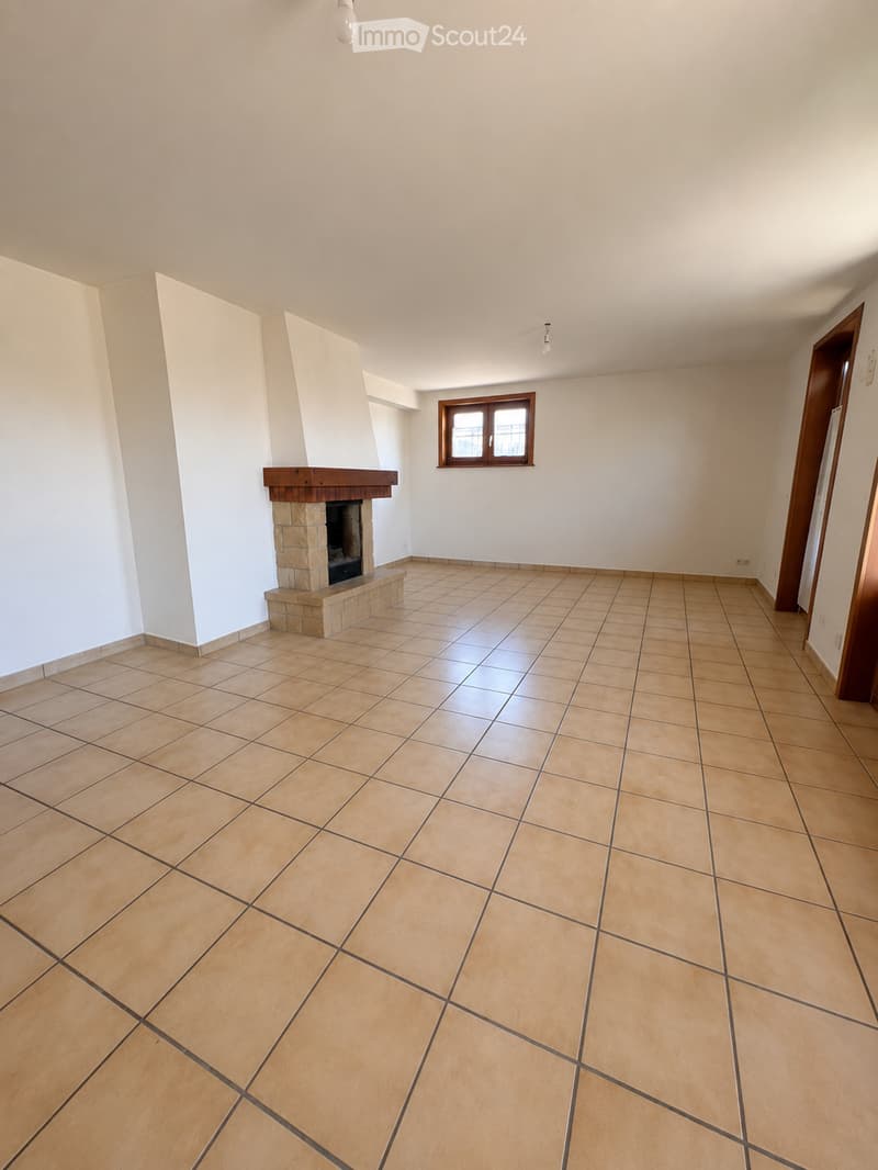 Empty room with tiled floor, white walls, and a fireplace with a wooden mantel. A window with brown frame is visible on one wall.