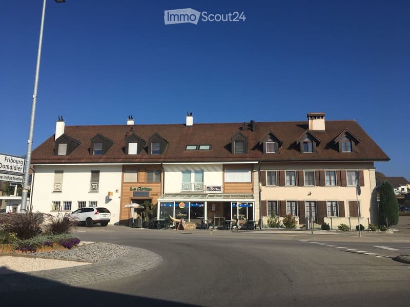 Two-story building with a brown tiled roof, multiple chimneys, and a restaurant area with outdoor seating and tables.