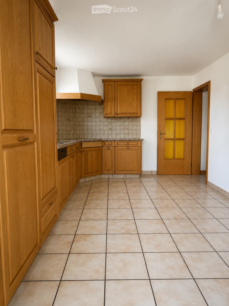 Empty kitchen with wooden cabinets, tiled floor, and a tiled backsplash. No appliances or furniture are present.