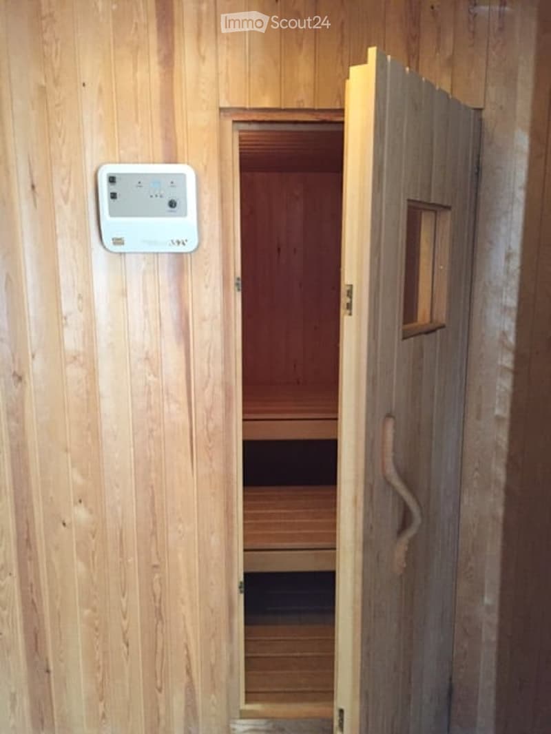 Wooden sauna with a control panel on the wall and an open door revealing the interior bench.