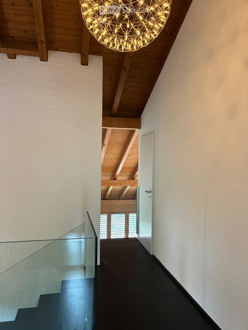 Modern hallway with wooden ceiling beams, glass railing, and a spherical light fixture.