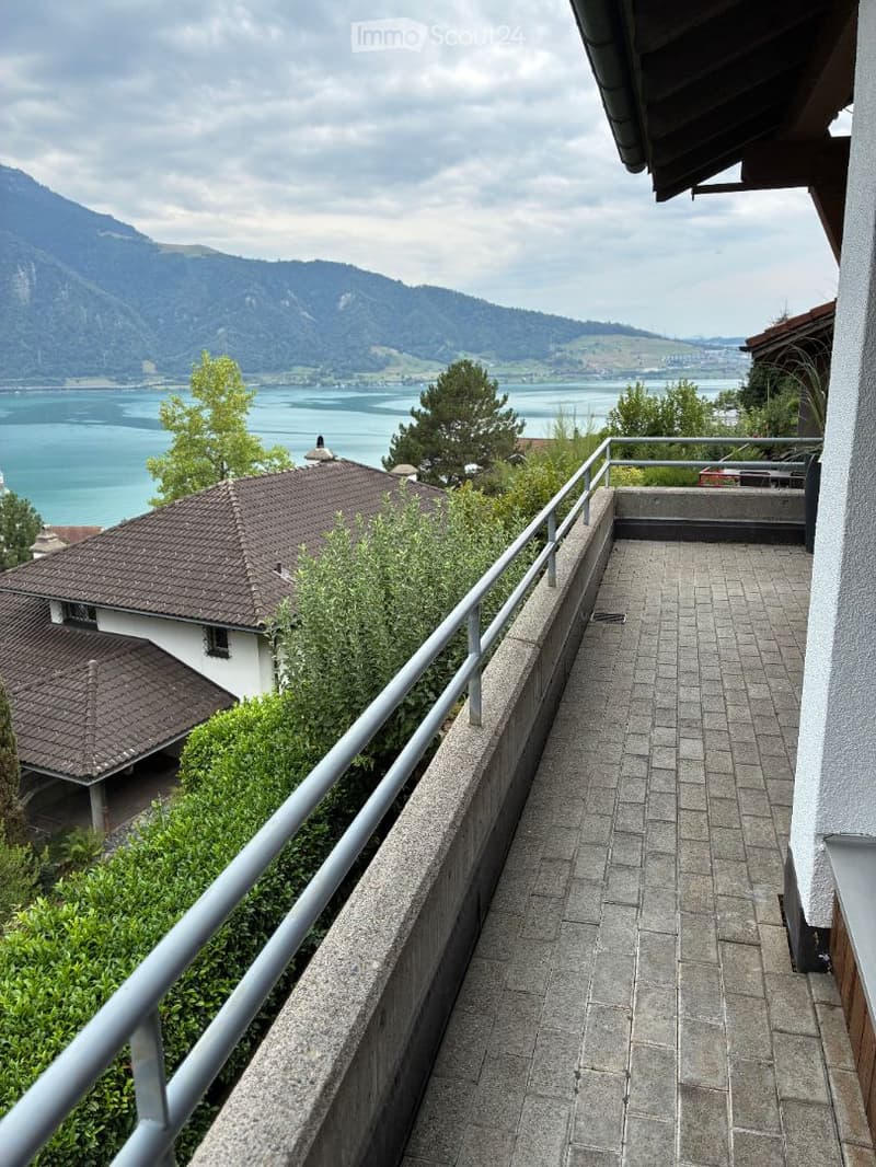 Balcony with a view of a lake and mountains, featuring a metal railing and tiled floor.
