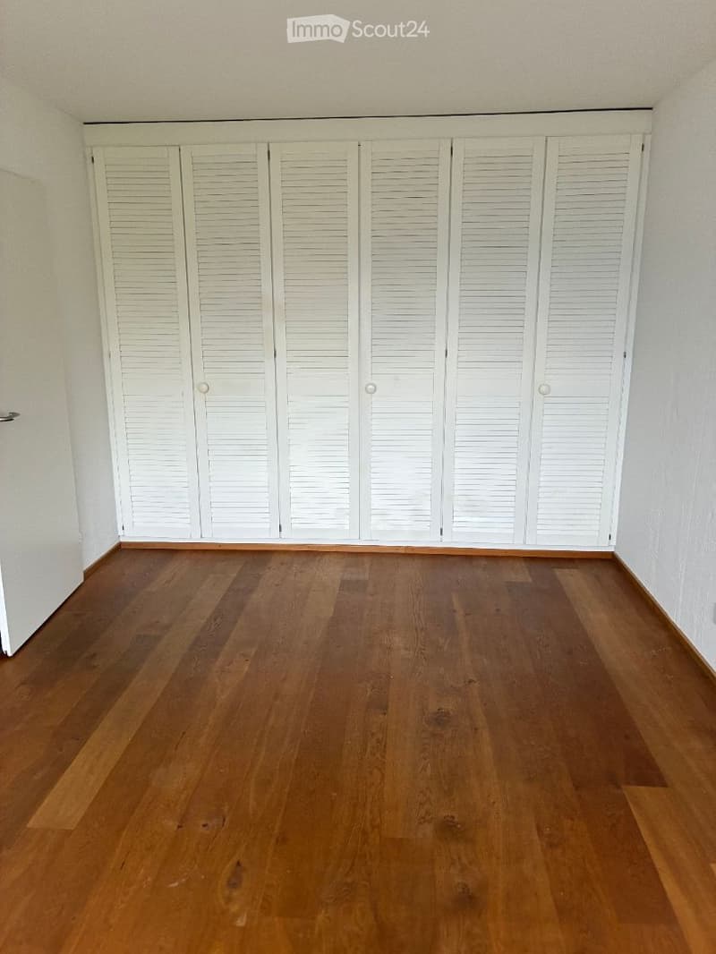 Empty room with wooden flooring and white louvered closet doors.