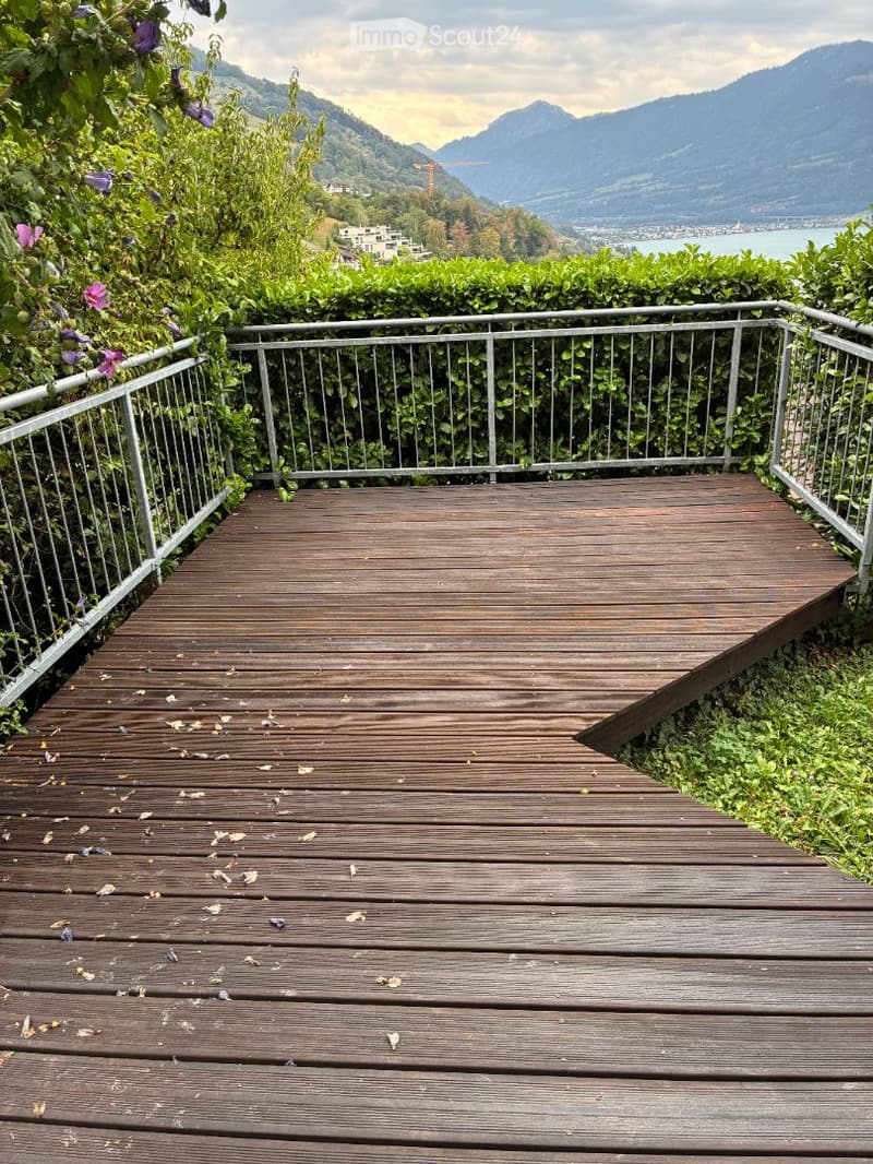Wooden deck with metal railing, overlooking a scenic mountain and lake view.