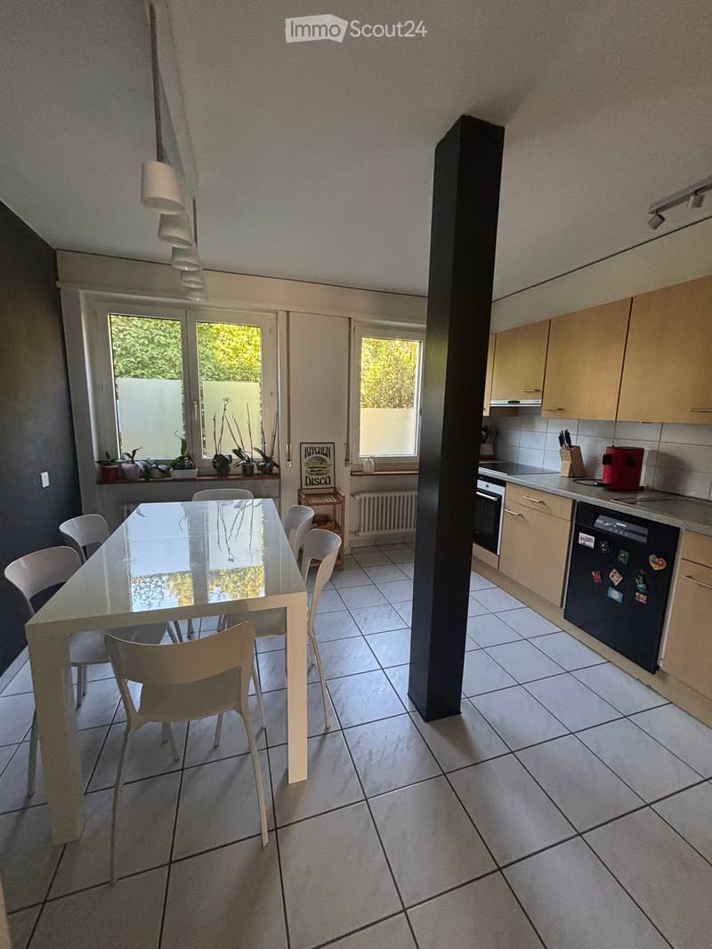 Modern kitchen and dining area with tiled flooring, light-colored cabinets, a glass dining table with chairs, and various appliances including a refrigerator, oven, and dishwasher.