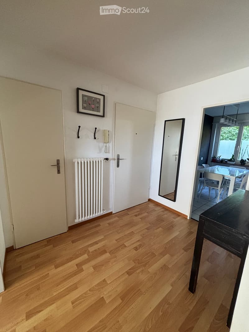 Hallway with wooden flooring, white walls, radiator, mirror, and a view into a dining area with a table and chairs.