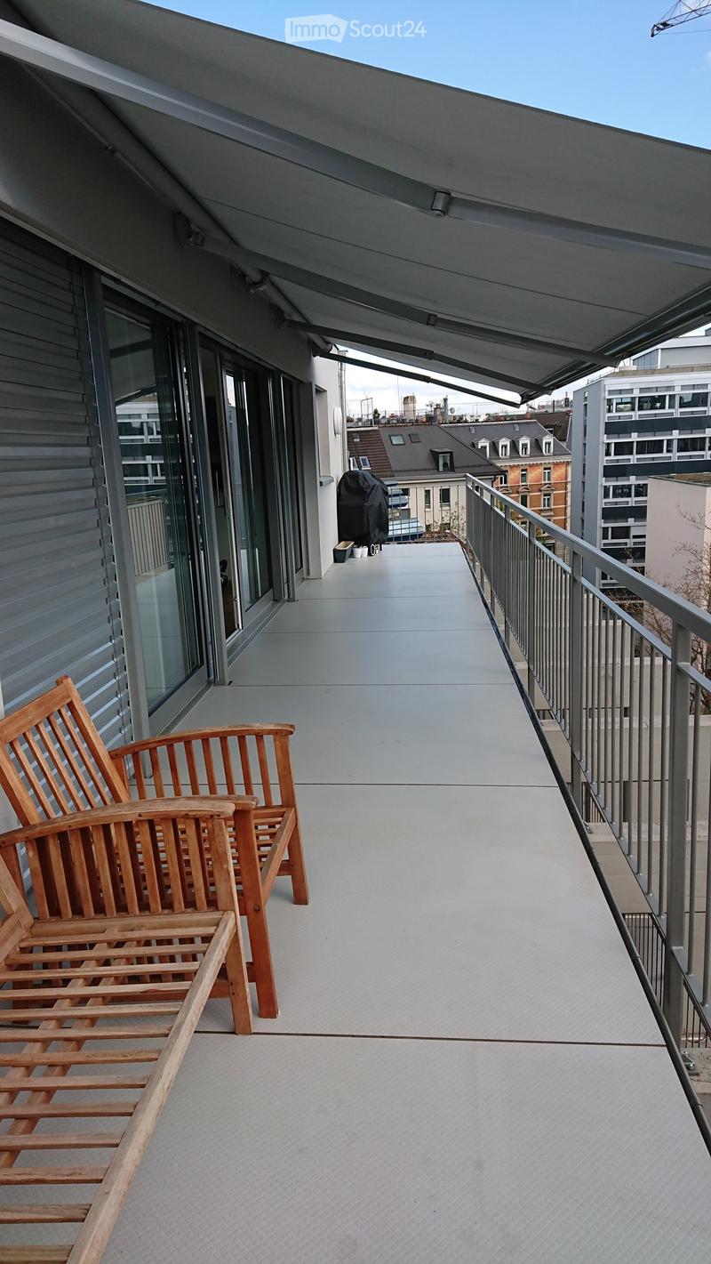 Balcony with wooden chairs, metal railing, and a covered area with glass doors leading to the interior.