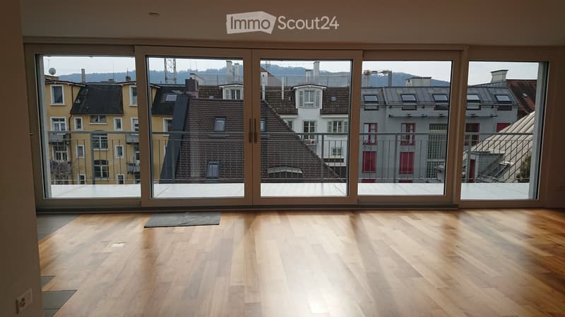 Empty room with wooden flooring and large sliding glass doors leading to a balcony with a cityscape view.