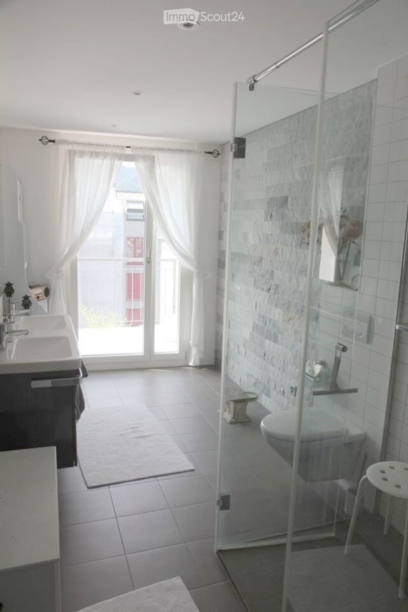 Modern bathroom with a glass-enclosed shower, double sink vanity, and a view through large windows.