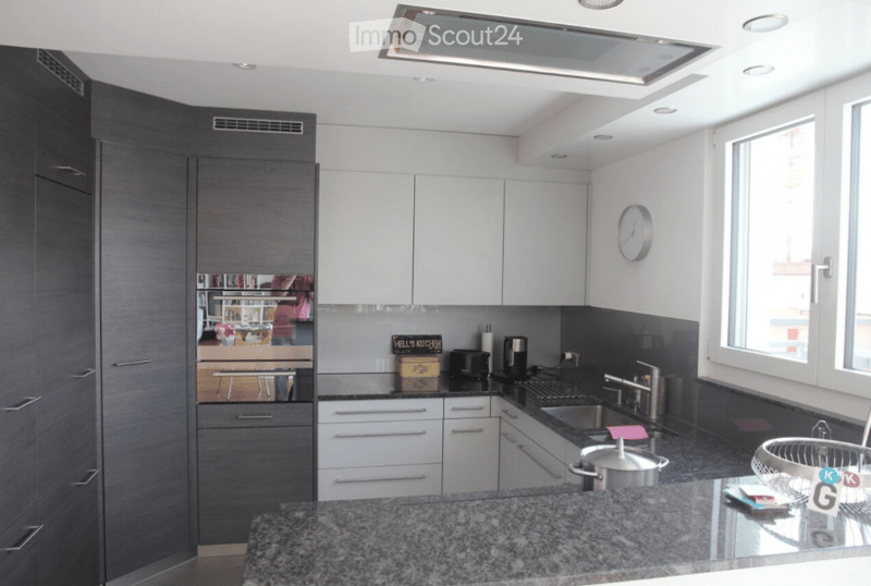 Modern kitchen with white cabinets, granite countertops, stainless steel sink, and various appliances including a coffee maker and oven. Features a large window and a built-in ventilation hood.