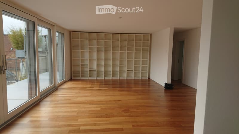 Empty room with wooden flooring, large glass sliding doors leading to a balcony, and a built-in shelving unit.