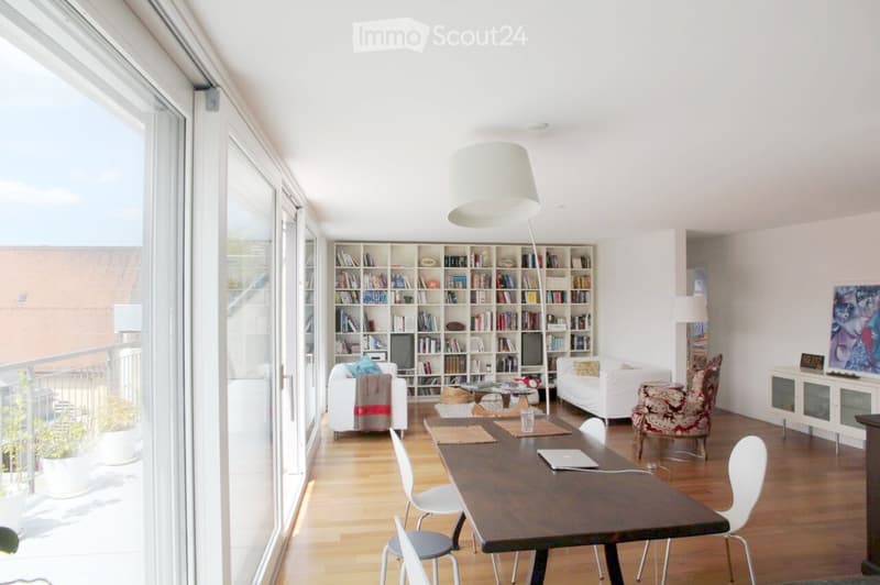 Bright living room with large windows and balcony access, featuring a wooden floor, white sofa, bookshelf, dining table, and modern decor.
