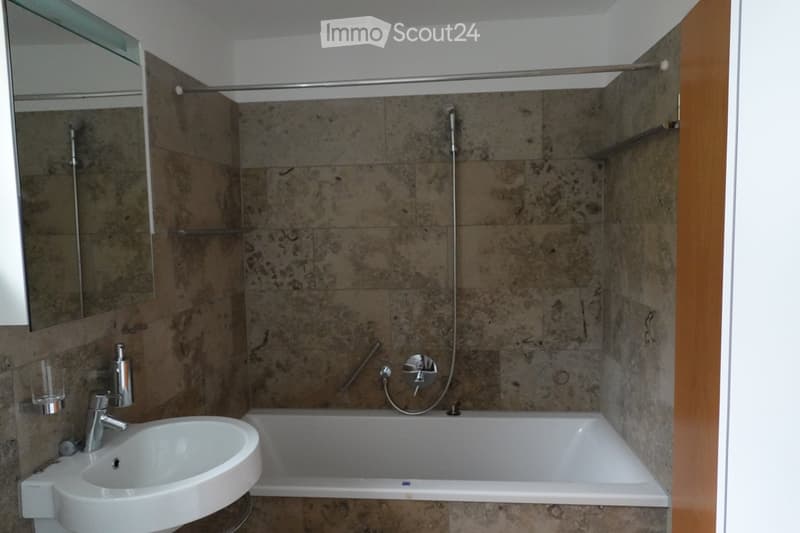Bathroom with marble tiles, white sink, bathtub, and shower area.