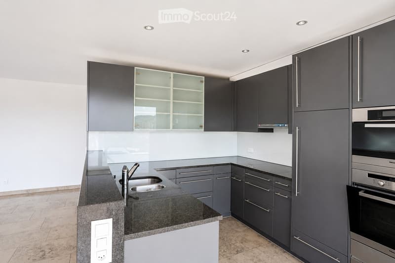 Modern kitchen with dark grey cabinets, granite countertop, stainless steel sink and faucet, and built-in oven.