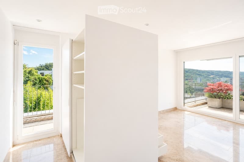 Bright, minimalist room with white walls, tiled floor, and large windows opening to a balcony with greenery and cityscape views.