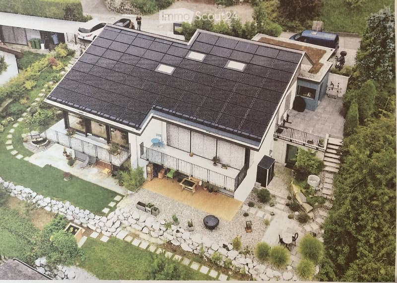 A modern house with a flat roof, solar panels, and a well-maintained garden with pathways and outdoor seating.
