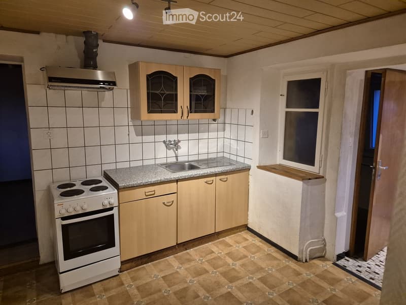 Compact kitchen with tiled walls, granite countertop, electric stove, sink, and wooden cabinets.