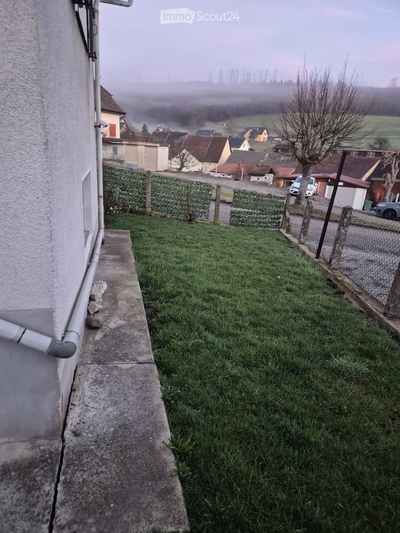 View of a grassy slope leading to a residential area with houses, a fence, and a road.
