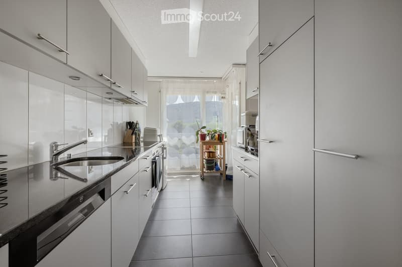 Modern kitchen with white cabinets, stainless steel sink, oven, microwave, and a small cart with plants and items.