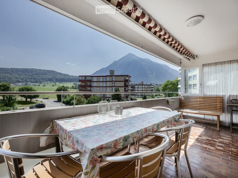 Balcony with a table, chairs, and a bench, overlooking a scenic mountain view.