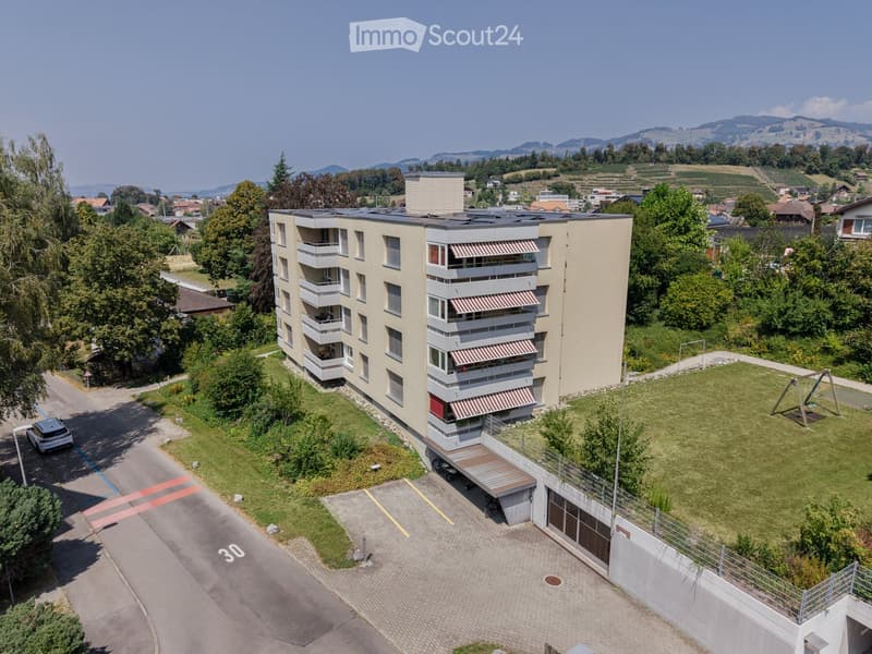A modern multi-story residential building with balconies, surrounded by greenery and a playground area.