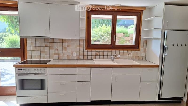 Bright kitchen with white cabinets, wooden countertops, and a large window overlooking a garden. Features an oven, refrigerator, and sink.