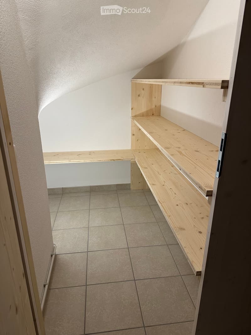 Empty room with wooden shelves built into the wall, tiled floor, and white walls.
