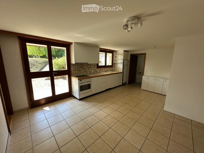 Empty kitchen with tiled floor, white cabinets, oven, refrigerator, and sink. Large sliding glass door provides access to outdoor area.