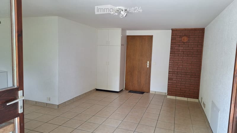 Empty hallway with tiled floor, white walls, a white cabinet, and a wooden door.