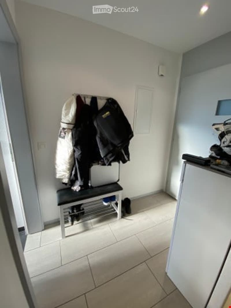 empty room with a bench, tile floor, and a few jackets hanging on the wall