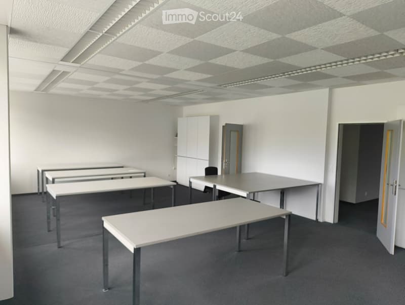 Office space with white tables, chairs, and a cabinet, featuring a gray carpet and white walls.