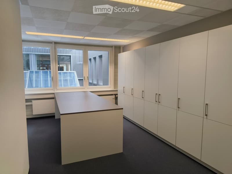 Office space with white cabinets, a grey table, and large windows.