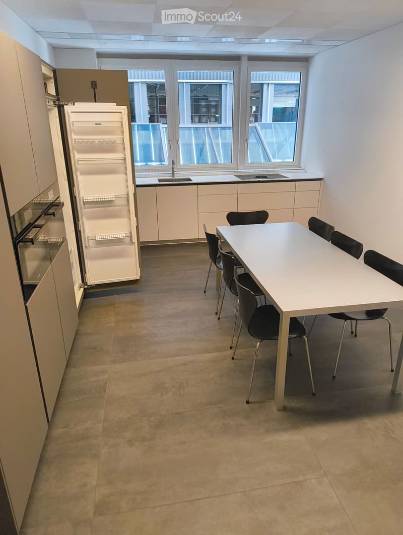 Modern kitchen with white cabinets, stainless steel appliances, a sink, and a dining area with a table and chairs.