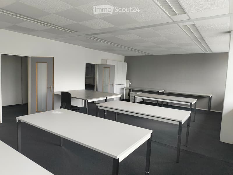 Modern office space with white tables, black chairs, and grey carpeting.