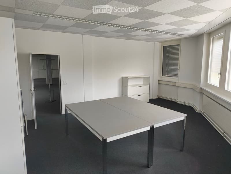 Office space with a large grey table, white cabinet, and a small open doorway leading to another room.