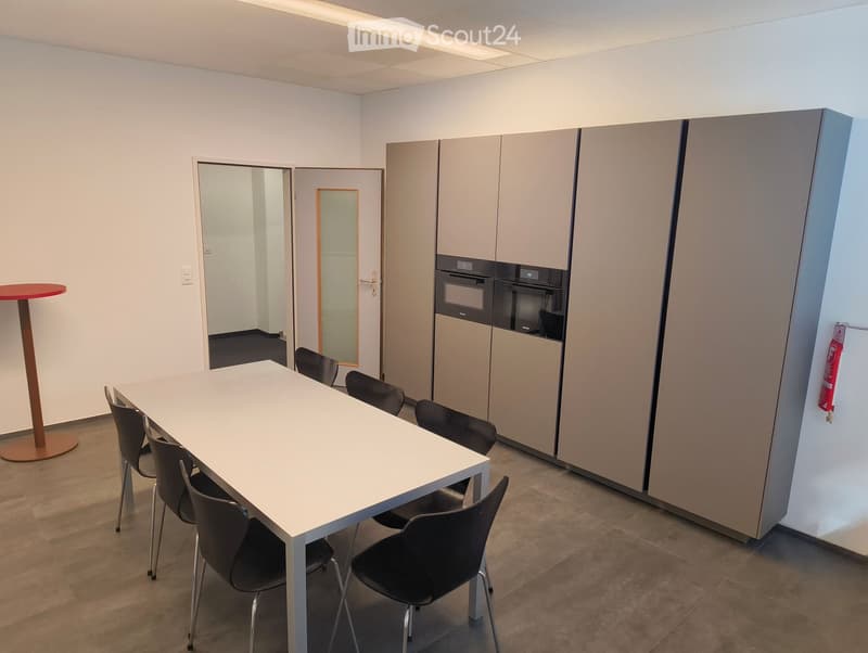 Modern, minimalist room with a white table surrounded by black chairs, a red round table on a stand, and built-in cabinets with an oven.
