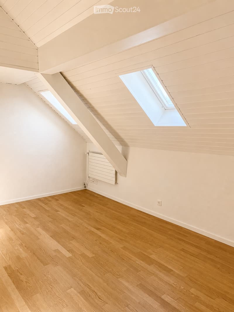 Empty attic room with wooden flooring, white walls, and skylight windows. No furniture or equipment present.