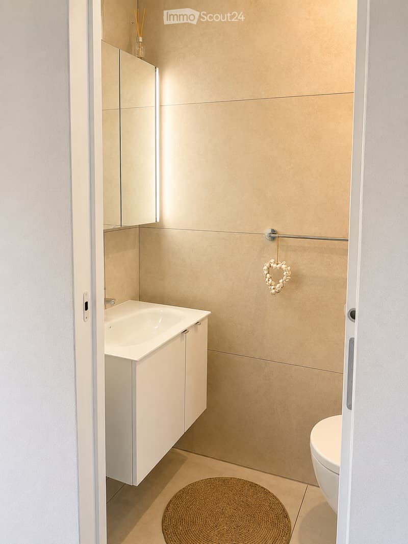 Modern bathroom with beige tiles, white sink cabinet, toilet, and a wicker basket on the floor.