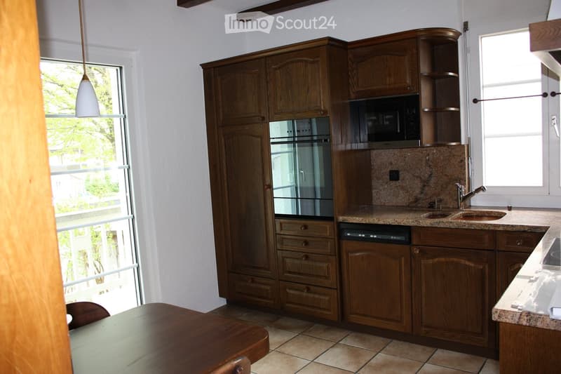 Well-lit kitchen with wooden cabinets, granite countertops, stainless steel appliances, and a dining area with a table and chairs.