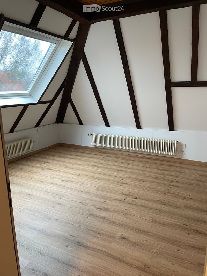 Empty attic room with wooden floors, white walls, exposed wooden beams, and a skylight window.