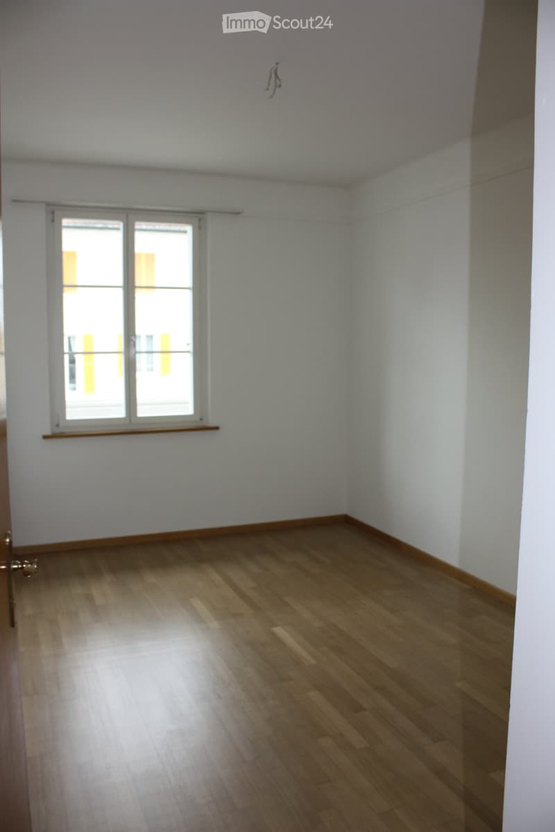 Empty room with wooden flooring, white walls, and a large window with blinds. No furniture or equipment is present.