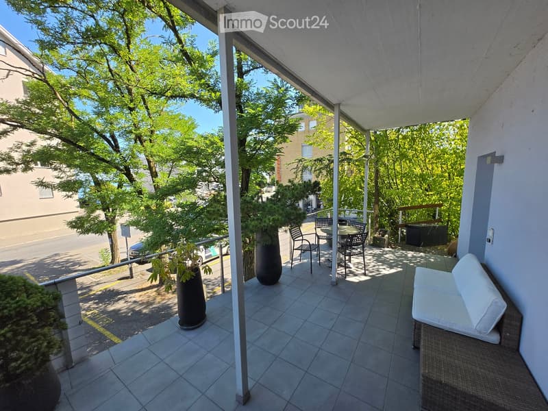 Balcony with tiled floor, white sofa, small table, chairs, and potted plants.
